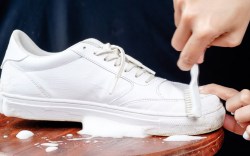 Woman cleaning white leather shoes with cleaning foam. The concept of caring for leather footwear