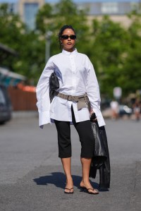 COPENHAGEN, DENMARK - AUGUST 7: A guest wears black sunglasses, white button up long sleeve shirt, black leather handbag, light brown belt, black capri pants, shiny black leather jacket, black flip flop kitten heels, outside Deadwood, during the Copenhagen Fashion Week Spring/Summer 2024-2025 on August 7, 2024 in Copenhagen, Denmark. (Photo by Edward Berthelot/Getty Images)