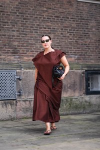 COPENHAGEN, DENMARK - AUGUST 7: A guest wears black sunglasses, dark red brown layered midi dress, dark brown flip flops, black leather bags, outside Mark Kenly Domino Tan, during the Copenhagen Fashion Week Spring/Summer 2024-2025 on August 7, 2024 in Copenhagen, Denmark. (Photo by Edward Berthelot/Getty Images)