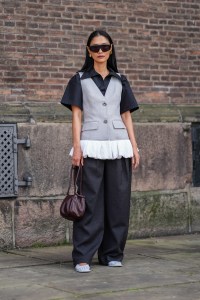 COPENHAGEN, DENMARK - AUGUST 7: Pornwika Spiecker wears black sunglasses, gold earrings, black short sleeve t-shirt, light gray tailored vest with white ruffled bottom, dark gray loose pants, shiny dark brown leather bag, white flat shoes, outside Mark Kenly Domino Tan, during the Copenhagen Fashion Week Spring/Summer 2024-2025 on August 7, 2024 in Copenhagen, Denmark. (Photo by Edward Berthelot/Getty Images)