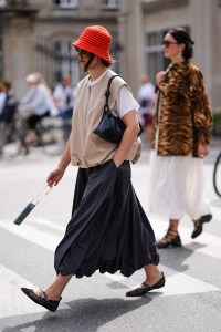 COPENHAGEN, DENMARK - AUGUST 8: A guest wears bright orange bucket hat, black sunglasses, white oversized t-shirt, light brown sleeveless puffy vest, black flowy skirt, shiny black leather bag, black sheer mesh ballerina flats, outside Gestuz, during the Copenhagen Fashion Week Spring/Summer 2024-2025 on August 8, 2024 in Copenhagen, Denmark. (Photo by Edward Berthelot/Getty Images)