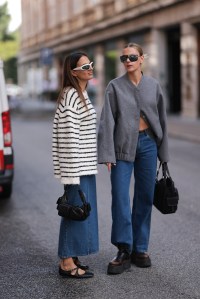 COPENHAGEN, DENMARK - AUGUST 08: Anna Winter (L) seen wearing white sunglasses, gold and silver necklaces, Edited white and black striped oversized boucle sweater, Edited blue denim long skirt, black leather bag and black leather ballet flats; Alessa Winter (R) wears black and gold sunglasses, gold earrings, Edited grey wool oversized bomber jacket, Edited blue denim long straight leg jeans, black leather and fabric bag and brown leather platform and plateau boots, during day four of the Copenhagen Fashion Week (CPHFW) SS25 on August 08, 2024 in Copenhagen, Denmark. (Photo by Jeremy Moeller/Getty Images)