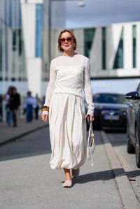 COPENHAGEN, DENMARK - AUGUST 8: A guest wears black sunglasses, gold earrings, white sheer mesh long sleeve shirt, dark brown black bangles, silver rings, cream flowy midi skirt, cream leather bag, white sheer mesh flats, outside Munthe, during the Copenhagen Fashion Week Spring/Summer 2024-2025 on August 8, 2024 in Copenhagen, Denmark. (Photo by Edward Berthelot/Getty Images)