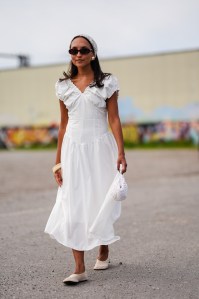 COPENHAGEN, DENMARK - AUGUST 5: A guest wears white head band, black sunglasses, gold earrings, white puffy sleeves tailored flowy midi dress, cream bangle, cream ring, white beaded bag, cream sandals, outside Rolf Ekroth, during the Copenhagen Fashion Week Spring/Summer 2024-2025 on August 5, 2024 in Copenhagen, Denmark. (Photo by Edward Berthelot/Getty Images)