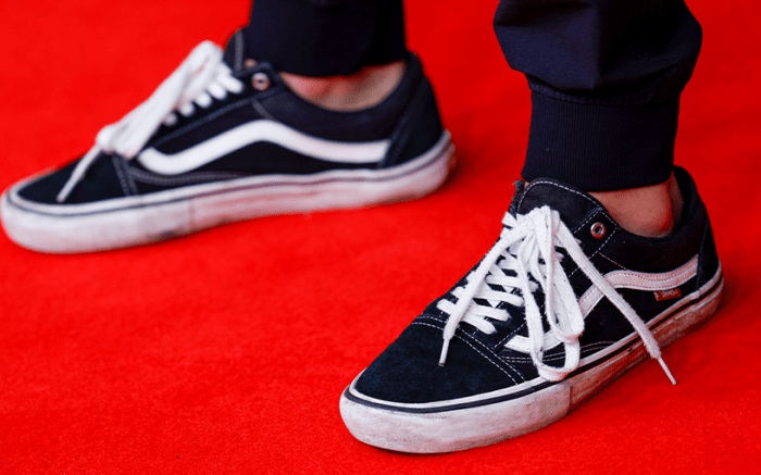 person wearing black and white Vans sneakers on a red carpet